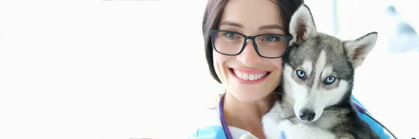 Mulher veterinário segurando cão com olhos azuis contra o fundo clínica animal de estimação — Fotografia de Stock