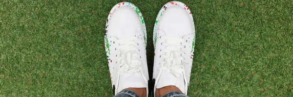 Mujeres piernas en vaqueros azules y blancas hermosas zapatillas de deporte en césped verde. — Foto de Stock