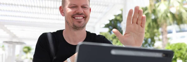 Retrato de homem sorridente acenando para tela tablet enquanto sentado fora em trópicos — Fotografia de Stock