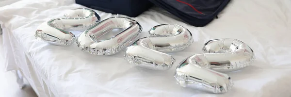 Silver balloons with numbers 2022 lying on bed with suitcase in bedroom closeup — Stock Photo, Image