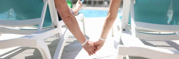 Hombre y mujer tumbados en tumbonas cerca de la piscina y tomados de las manos de cerca — Foto de Stock