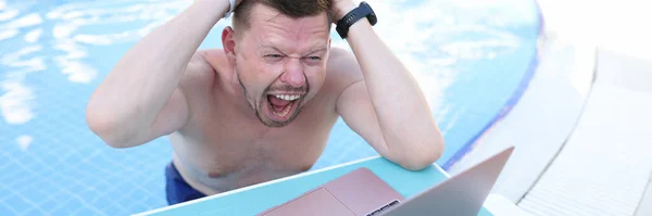 Homem gritando e segurando seu cabelo e olhando para a tela do laptop no lado da piscina — Fotografia de Stock