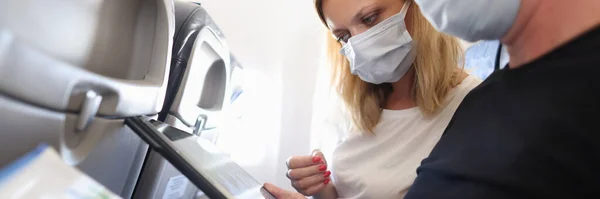 Hombre y mujer en máscaras protectoras volando en avión y mirando la pantalla de la tableta digital y documentos con gráficos — Foto de Stock