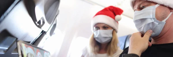 Hombre y mujer en máscaras médicas protectoras y sombreros de Santa Claus celebrando la Navidad con amigos en línea en el avión — Foto de Stock