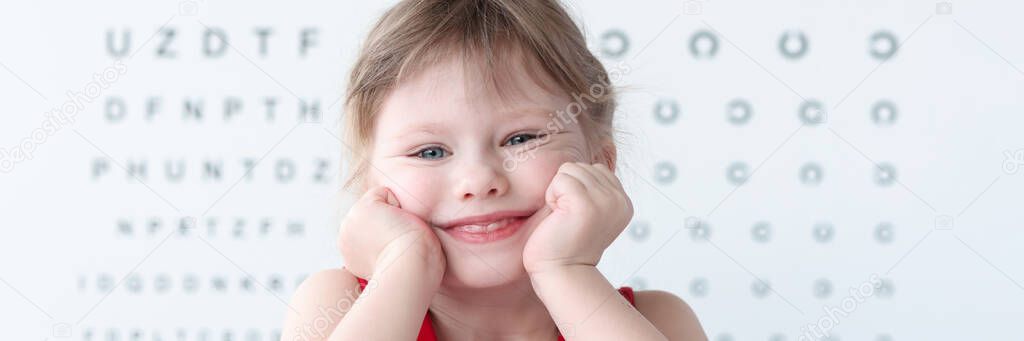 Smiling little child against vision test table in medical clinic portrait