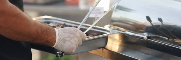 Szef kuchni w gumowych rękawiczkach trzyma metalową tacę z jedzeniem i szczypcami zbliżenie — Zdjęcie stockowe