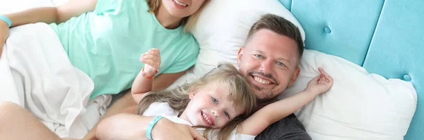 Young man and woman lying with little girl in bed — Stock Photo, Image