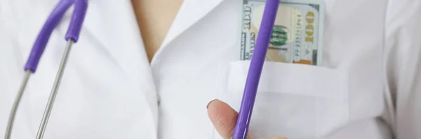 Doutor com notas de dólar no bolso segurando estetoscópio close-up — Fotografia de Stock