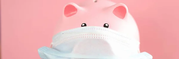 Pink pig piggy bank in protective mask and stethoscope stands on table