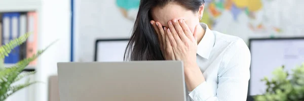Triste giovane donna siede al computer portatile coprendo il viso con le mani — Foto Stock