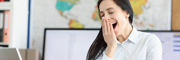 Молодая женщина зевает на рабочем месте за ноутбуком