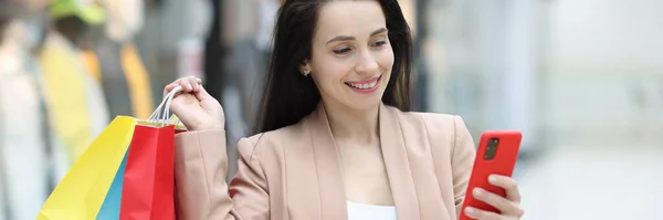 Donna sorridente tiene in mano smartphone e acquisti nel centro commerciale — Foto Stock