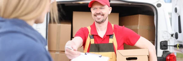 Smiling male courier hands over clipboard with pen to woman to sign receipt of parcel — Stock Photo, Image