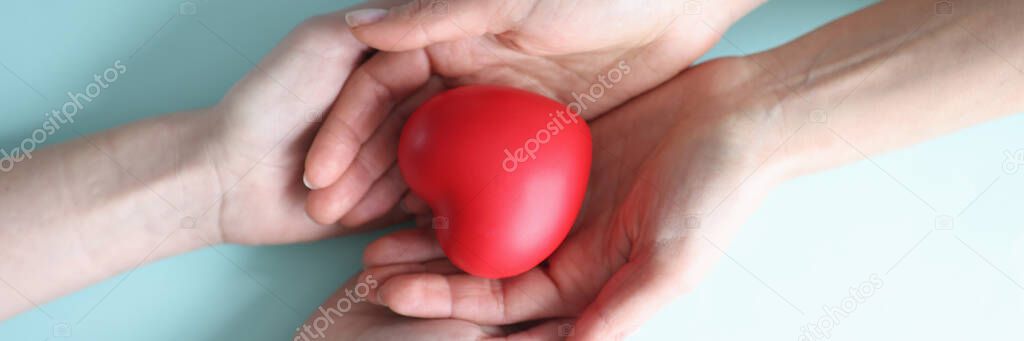 Small red heart lies in hands of two people