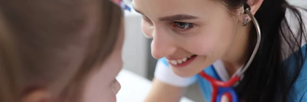 Pediatrician doctor listening to heart of little girl with stethoscope in clinic