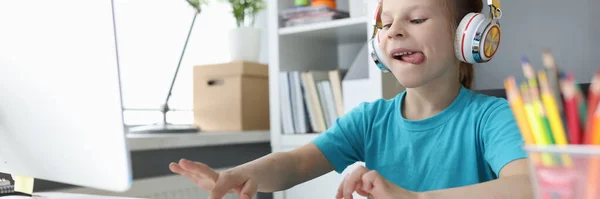 Niña en auriculares sentada en la mesa y escribiendo en el teclado de la computadora —  Fotos de Stock