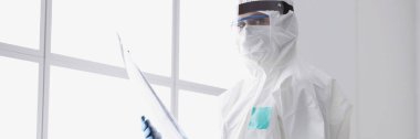Koruyucu giysili ve maskeli doktor röntgen cihazı tutuyor.