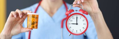 Gülen doktor elinde kırmızı çalar saat ve ilaç tutuyor.