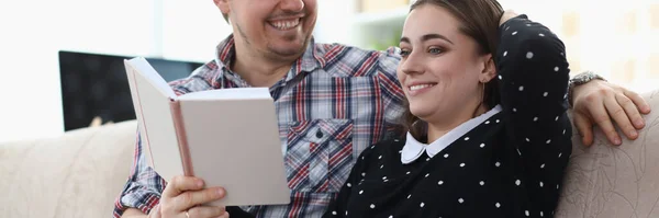 Sonriendo hombre y mujer están sentados en el sofá y sosteniendo el libro —  Fotos de Stock