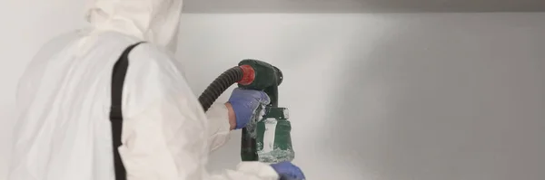 Master malarz w białym garniturze maluje ścianę pistoletem natryskowym — Zdjęcie stockowe
