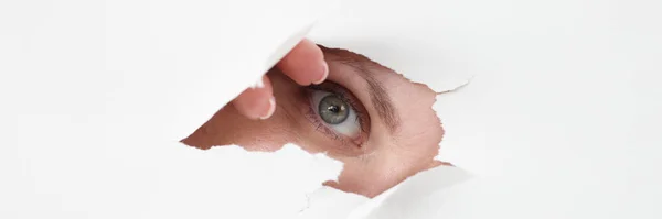 Женский глаз смотрит сквозь отверстие в белой бумаге — стоковое фото