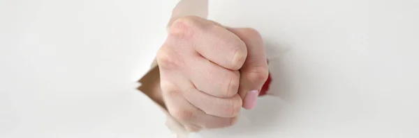 Tightly clenched fist through hole in white paper — Stock Photo, Image