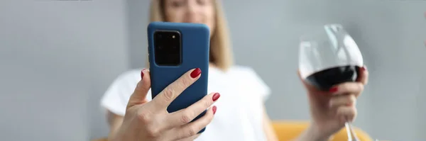 Mulher olha para o smartphone e segura copo de vinho na mão — Fotografia de Stock