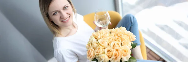 Donna sorridente che tiene in mano un bicchiere di vino e un mazzo di fiori — Foto Stock