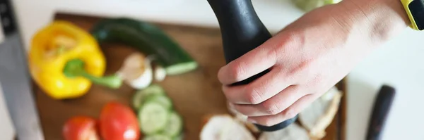 Mãos de cozinheiro derramando pimenta do moinho em carne e legumes close-up — Fotografia de Stock