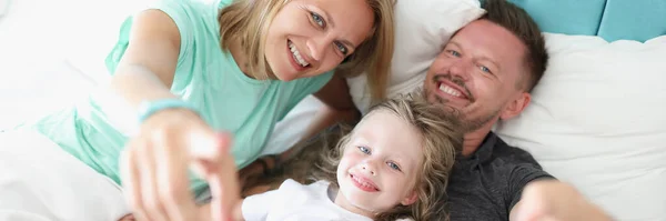 Menina e pais deitados na cama e sorrindo — Fotografia de Stock