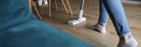 Woman cleaning floor in apartment with vacuum cleaner closeup