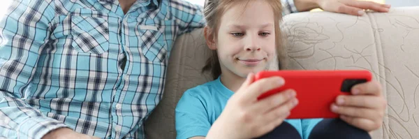 Bambina e madre sono seduti sul divano con il telefono cellulare in mano — Foto Stock