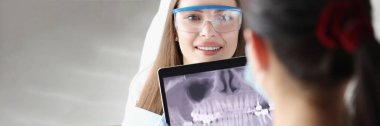 Klinikte kadın hastaların önünde dijital tablet ve panoramik çene fotoğrafı tutan dişçi