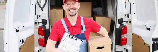 Man courier holding delivery documents and cardboard box near car — Stock Photo, Image