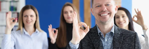 Бизнесмен показывает нормальный жест на фоне коллег в офисе — стоковое фото