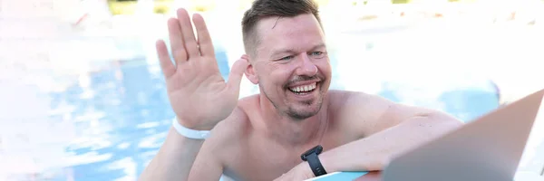 Retrato de homem emocionalmente sorridente acenando com a mão para a webcam do laptop enquanto estava na piscina — Fotografia de Stock