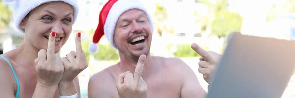 Hombre y mujer alegre en sombreros rojos de Santa Claus muestran gesto de hecho en monitor portátil estar en el complejo en la piscina —  Fotos de Stock