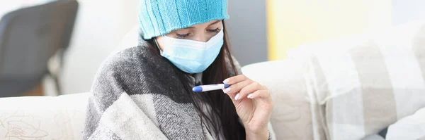 Femme en casquette et masque médical de protection regardant thermomètre — Photo