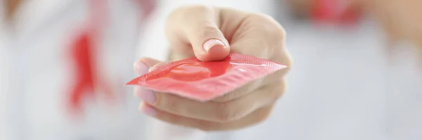 Läkare som håller röd kondom på kliniken närbild — Stockfoto