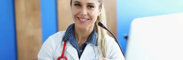 Молодая женщина врач сидит за столом перед микрофоном — стоковое фото