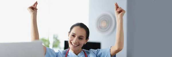 Glimlachende vrouw arts zitten aan tafel en het verhogen van haar handen omhoog — Stockfoto