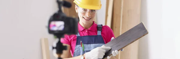 Woman builder in safety helmet holding wooden board in front of camera — Stock Photo, Image