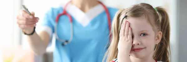 Маленькая девочка закрывает глаза рукой на приеме у офтальмолога — стоковое фото