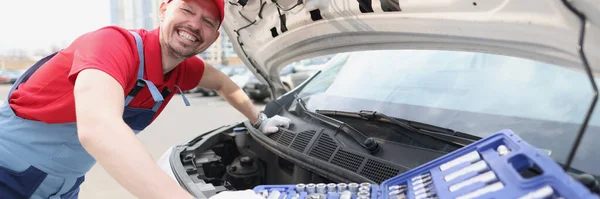 Smiling repairman in uniform fixing car with tools — стоковое фото