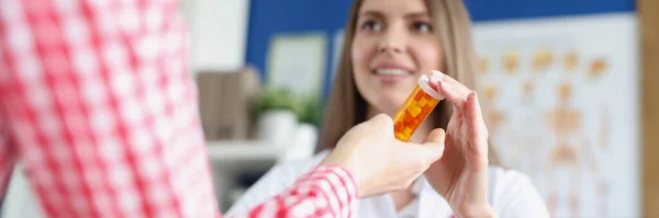 Woman doctor giving jar of capsules to patient in hands in clinic closeup — Stockfoto
