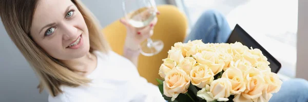 Young woman with bouquet of tea roses sitting at laptop with glass of white wine — Stock Photo, Image