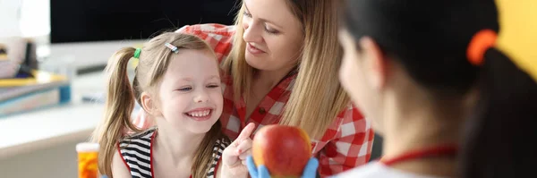 Läkare som erbjuder liten flicka flaska medicin och rött äpple på kliniken — Stockfoto