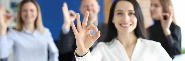 Бізнес-леді показує нормальний жест на тлі колег в офісі крупним планом — стокове фото