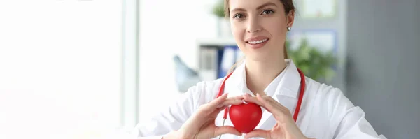 Glimlachende vrouw arts met rood speelgoed hart in haar handen in de kliniek — Stockfoto