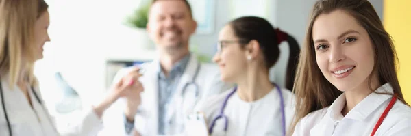 Mujer sonriente médico con estetoscopio rojo de pie sobre el fondo de los colegas — Foto de Stock